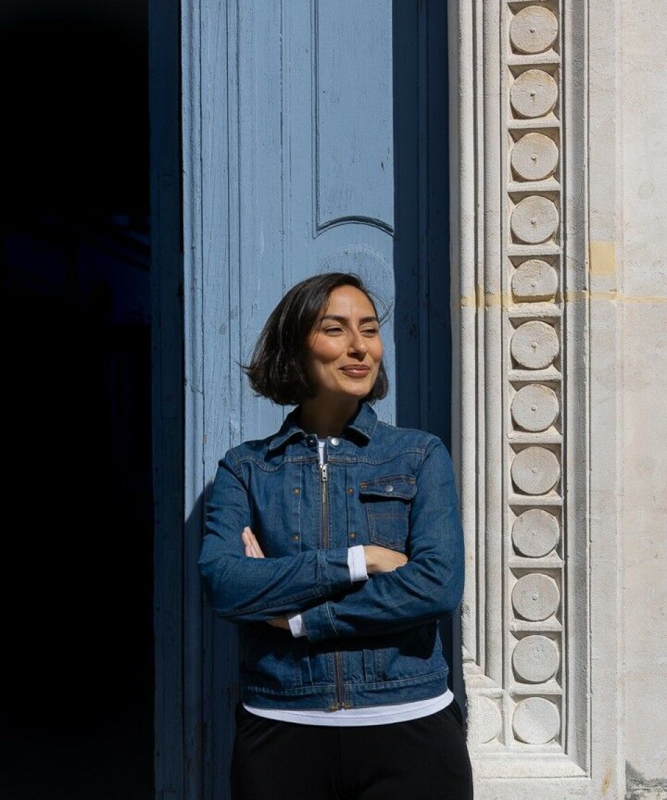 Jeune femme souriante, debout devant la porte d'entrée, les bras croisés
