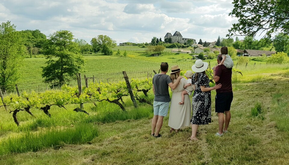 Groupe de personnes sur une colline herbeuse surplombant les vignobles verdoyants et les bâtiments de ferme