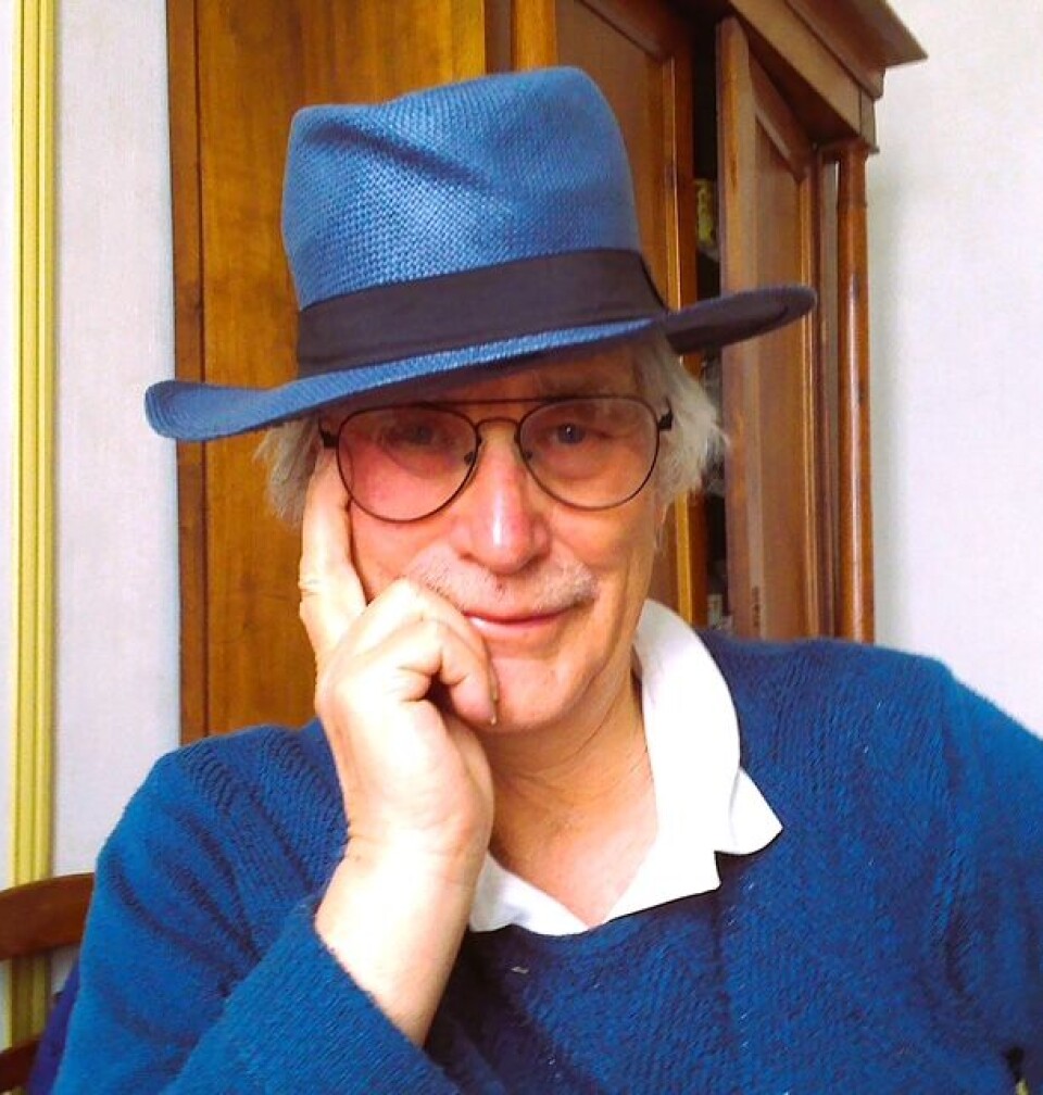 Homme au chapeau bleu et aux lunettes posant à l'intérieur, posant son menton sur sa main.