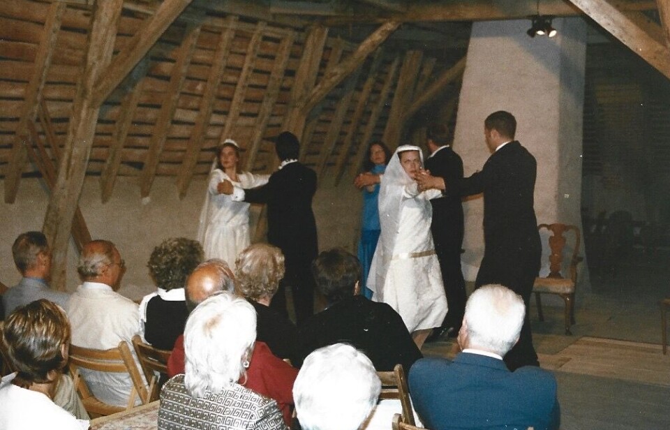 Les invités du mariage assis dans une salle rustique regardent une cérémonie à l’avant de la salle.