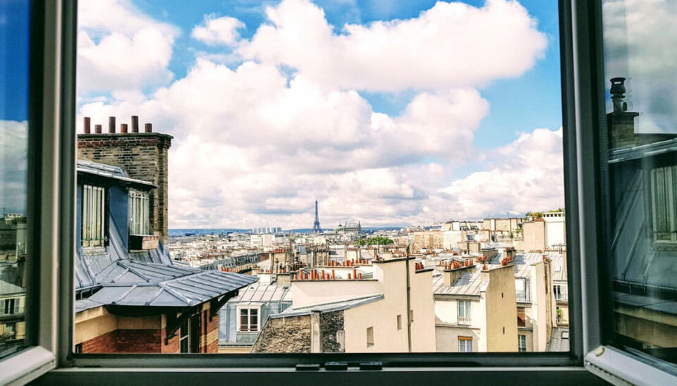 Fenêtres ouvertes encadrant les toits et les toits d'une ville lointaine sous les nuages.
