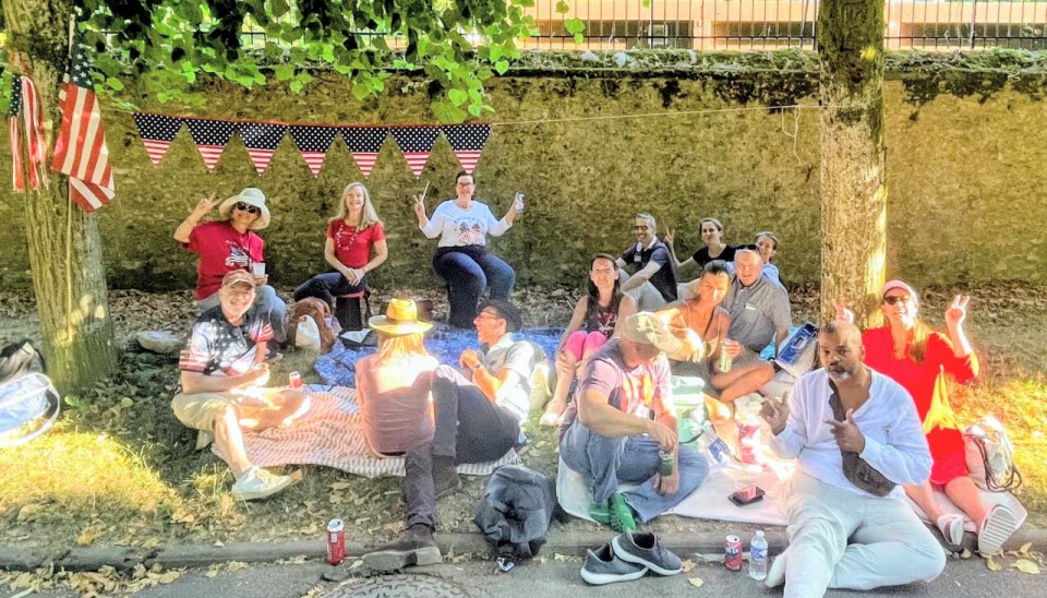Groupe de personnes assises sur des couvertures et des chaises lors d'un pique-nique en plein air sous les arbres avec des banderoles au-dessus.