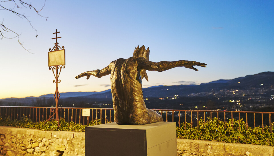 Statue en bronze aux bras tendus surplombant une vallée de montagne