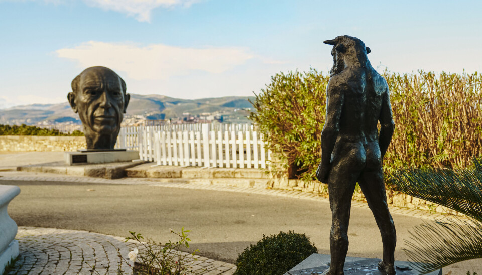 Statue en bronze sur une promenade en bord de mer avec une deuxième sculpture et un paysage côtier derrière elle