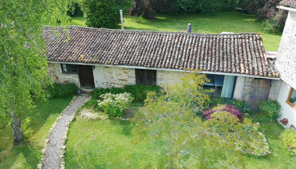 Dépendance en pierre patinée avec un toit de tuiles à côté d'une allée de jardin et de plantes à fleurs