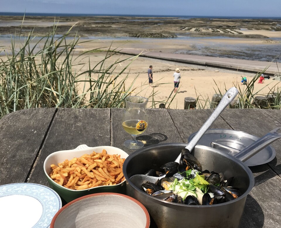 Marmite de moules, chips et bols de nourriture sur une table en bord de mer surplombant une plage