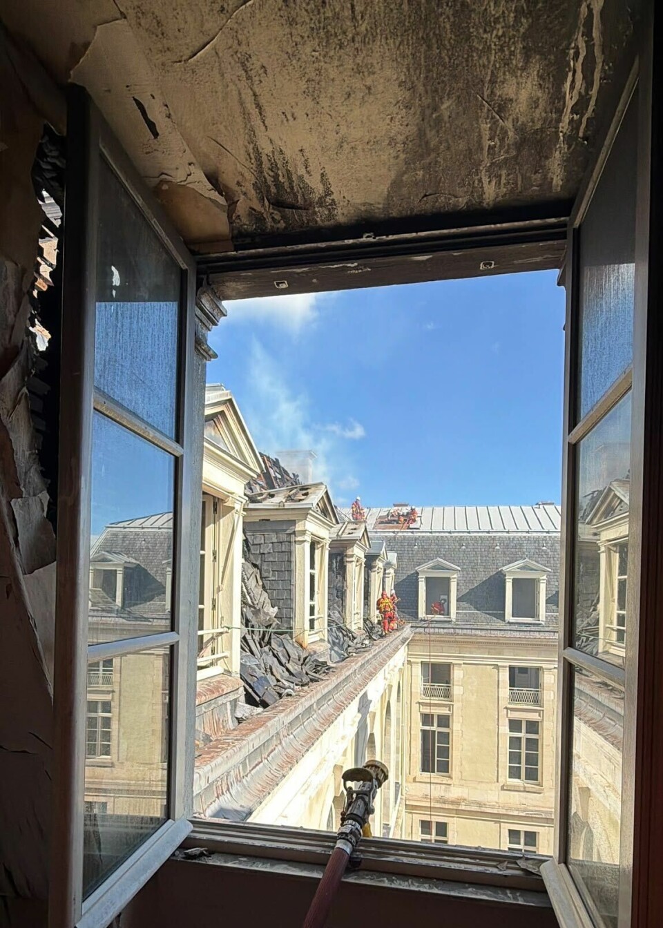 Pièce carbonisée encadrant une fenêtre ouverte donnant sur des bâtiments historiques aux toits d'ardoise