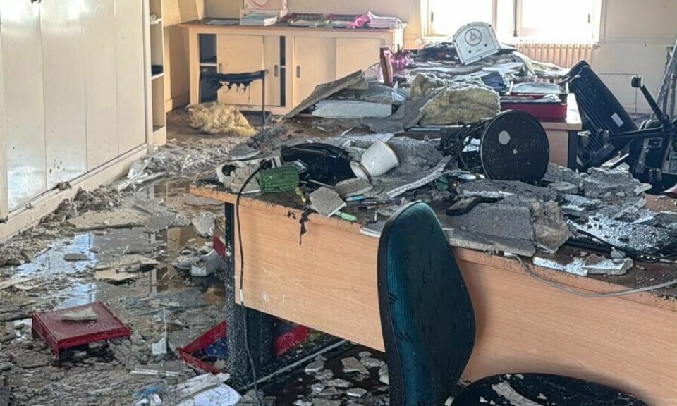 Pièce endommagée avec décombres, chaises renversées, bureaux cassés et plafond apparent
